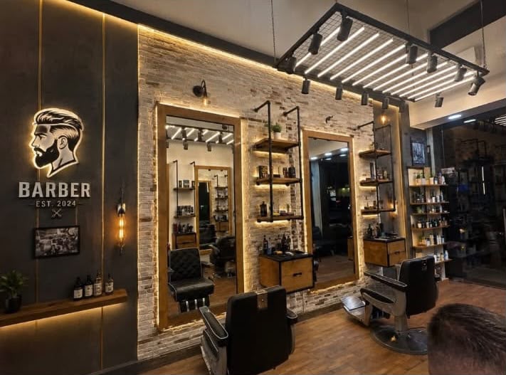 The Ahmad Al Shami barbershop interior — warm lighting, stone-clad wall, leather chairs, mirrors and the illuminated BARBER sign
